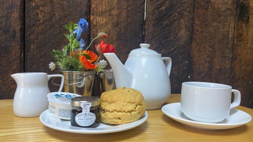 A teapot, teacup, scone with cream and jam on a table with a floral arrangement